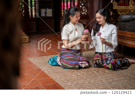 Two charming Asian women sitting in a temple and enjoying folding lotus flowers together. 120129421