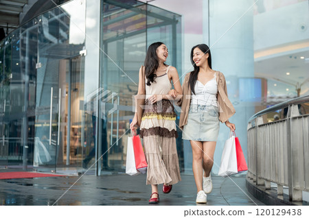 Two attractive Asian female friends enjoy a fun weekend shopping day at the mall, walking out. 120129438