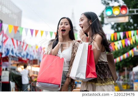 Cheerful Asian female friends are excited and amazed by the various food stalls at a night market. Cheerful Asian female friends are excited and amazed by the various food stalls at a night market. 120129476