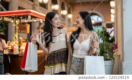 Two charming Asian female friends enjoy shopping together at a mall or night market. 120129514
