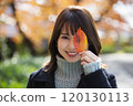 大阪府大阪市宮古島區櫻之宮公園,秋葉背景下,一位微笑的年輕女子用樹葉遮住一隻眼睛 大阪府大阪市宮古島區櫻之宮公園,秋葉背景下,一位微笑的年輕女子用樹葉遮住一隻眼睛 120130113