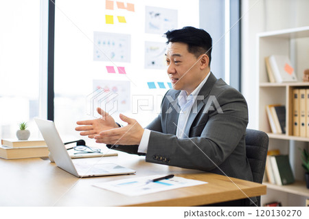 Asian businessman conducting online meeting in modern office setting 120130270