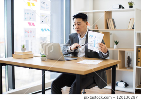 Asian businessman in headset conducts online presentation with graphs Asian businessman in headset conducts online presentation with graphs 120130287
