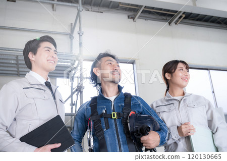 穿著工作服的總承包商和穿著牛仔布的現場主管等三人，抬頭看著現場的 IT 和 DX。 120130665