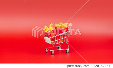 Supermarket trolley, with red gifts. Buying gifts for Sale, Discounts, Black Friday, New Year, Christmas, Birthday and Valentines day. On a red background, minimal design 120132254