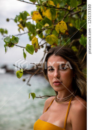 A beautiful portrait showcasing a young woman standing by the ocean amidst tropical foliage 120133380