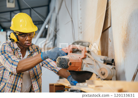 Construction worker in a yellow helmet using a chop saw to cut wood, with a vacuum cleaner collecting wood chips. woodworking, precision cutting, and construction sites, National Carpenters Day 120133631