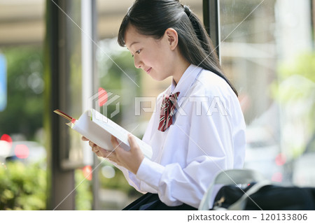 A female junior high school student reading a textbook at a bus stop 120133806