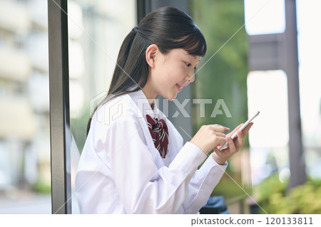 A female junior high school student looking at her smartphone at a bus stop A female junior high school student looking at her smartphone at a bus stop 120133811