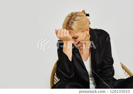 A woman is crying while sitting dramatically in a chair, captured in a bright indoor setting 120135033