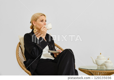 Woman enjoying tea in a minimalist setting while seated on a rattan chair during the day Woman enjoying tea in a minimalist setting while seated on a rattan chair during the day 120135036