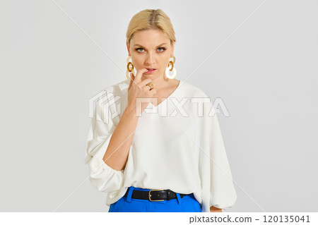 A woman poses thoughtfully in a white blouse and blue pants, showcasing a modern fashion style A woman poses thoughtfully in a white blouse and blue pants, showcasing a modern fashion style 120135041