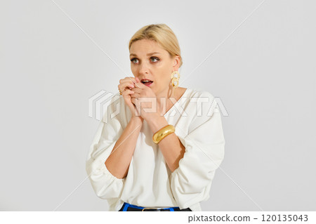 Woman nervously biting nails while expressing surprise in a bright studio setting during the daytime 120135043