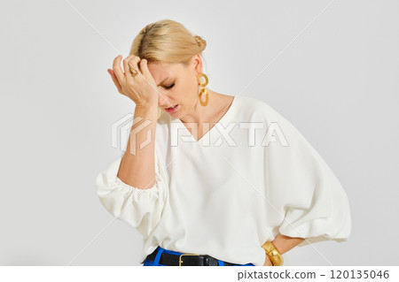 A woman in a white blouse expresses frustration while standing against a plain background 120135046