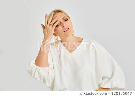 A woman in a white blouse shows signs of stress while posing in a minimalistic studio setting 120135047
