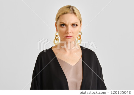 A woman with blond hair and bold earrings poses confidently against a neutral backdrop A woman with blond hair and bold earrings poses confidently against a neutral backdrop 120135048
