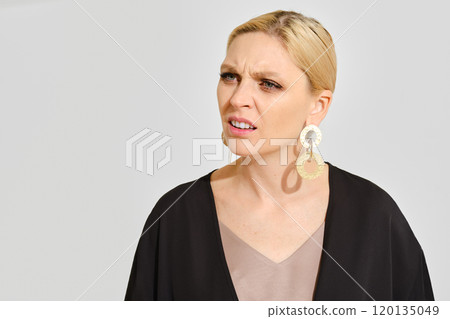 Confused woman with statement earrings expresses puzzlement in a minimalist setting 120135049