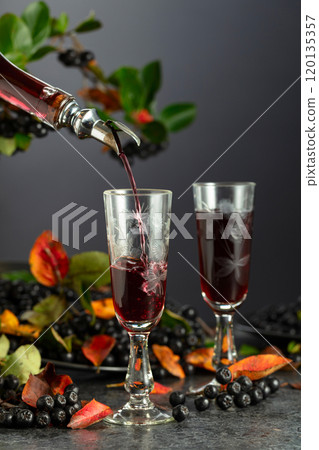 Black chokeberry drink is poured from a bottle into a glass. 120135357