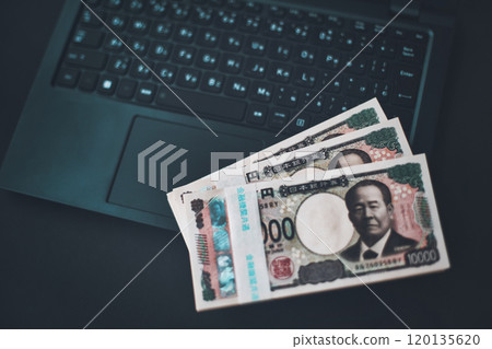 A stack of Japanese yen bills and an open laptop 120135620
