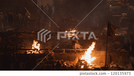 Varanasi, Uttar Pradesh, India. Cremation in process on Manikarnika Ghat. Cinematic Camera movement moving along riverbank embankment. View from riverside. night lights. Fire, smoke - Funeral rites of Varanasi, Uttar Pradesh, India. Cremation in process on Manikarnika Ghat. Cinematic Camera movement moving along riverbank embankment. View from riverside. night lights. Fire, smoke - Funeral rites of 120135973