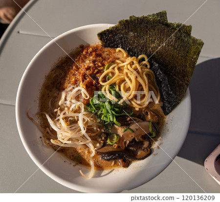 Vegan ramen closeup. Asian noodles with mushrooms, nori and greens, vegan dish in sunlight, street restaurant, blurred background Vegan ramen closeup. Asian noodles with mushrooms, nori and greens, vegan dish in sunlight, street restaurant, blurred background 120136209