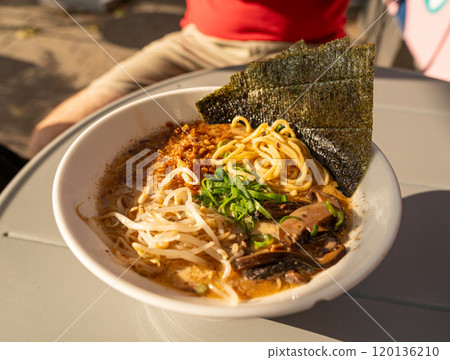 Vegan ramen closeup. Asian noodles with mushrooms, nori and greens, vegan dish in sunlight, street restaurant, blurred background Vegan ramen closeup. Asian noodles with mushrooms, nori and greens, vegan dish in sunlight, street restaurant, blurred background 120136210