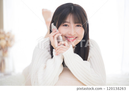 Close-up of a young cute girl talking on her smartphone while lying face down, looking at the camera Close-up of a young cute girl talking on her smartphone while lying face down, looking at the camera 120138263