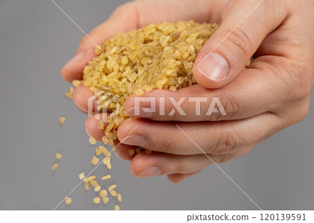 Hands pouring raw uncooked bulgur cereals on a gray background. Hands pouring raw uncooked bulgur cereals on a gray background. 120139591