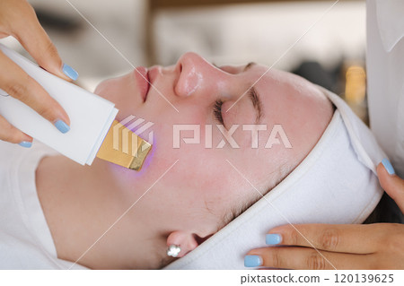 A professional skincare specialist applies a cooling gel on a client's face with a gentle spatula, focusing on precise treatment. A professional skincare specialist applies a cooling gel on a client's face with a gentle spatula, focusing on precise treatment. 120139625