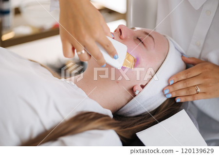 A professional skincare specialist applies a cooling gel on a client's face with a gentle spatula, focusing on precise treatment. 120139629
