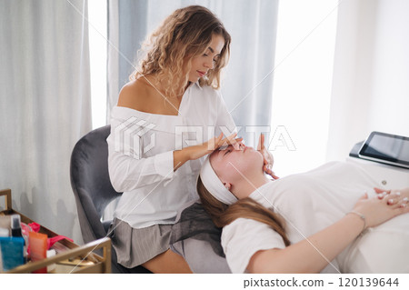 Close-up of a beauty specialist's hands applying a soothing facial cream on a client's cheek with a gentle massage Close-up of a beauty specialist's hands applying a soothing facial cream on a client's cheek with a gentle massage 120139644