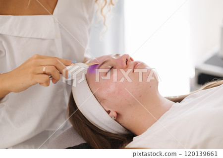 A professional skincare specialist applies a cooling gel on a client's face with a gentle spatula, focusing on precise treatment. A professional skincare specialist applies a cooling gel on a client's face with a gentle spatula, focusing on precise treatment. 120139661