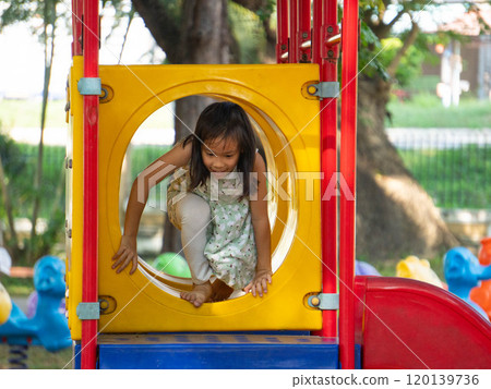 Cute girl having fun on a colorful slide in an outdoor park. Children playing in the playground during summer vacation. 120139736