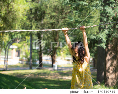 Cute sisters are having fun hanging from ropes in an outdoor park. Children playing in the playground during summer vacation. Cute sisters are having fun hanging from ropes in an outdoor park. Children playing in the playground during summer vacation. 120139745