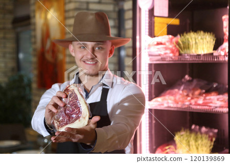 The waiter holds a large raw steak in his hands. Demonstration of steaks in a restaurant. The chef offers a steak in a package. The cook took a steak out of the refrigerator. 120139869