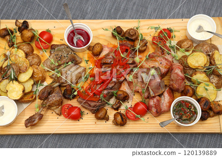 A large wooden board with appetizers: duck, steaks, mushrooms, tomatoes and various sauces for four people. A huge wooden board with excellent meat and vegetable appetizers. A large wooden board with appetizers: duck, steaks, mushrooms, tomatoes and various sauces for four people. A huge wooden board with excellent meat and vegetable appetizers. 120139889
