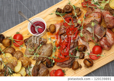 A large wooden board with appetizers: duck, steaks, mushrooms, tomatoes and various sauces for four people. A huge wooden board with excellent meat and vegetable appetizers. A large wooden board with appetizers: duck, steaks, mushrooms, tomatoes and various sauces for four people. A huge wooden board with excellent meat and vegetable appetizers. 120139891