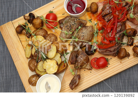 A large wooden board with appetizers: duck, steaks, mushrooms, tomatoes and various sauces for four people. A huge wooden board with excellent meat and vegetable appetizers. A large wooden board with appetizers: duck, steaks, mushrooms, tomatoes and various sauces for four people. A huge wooden board with excellent meat and vegetable appetizers. 120139892
