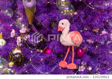 Pink flamingo on purple Christmas tree. Soft funny children's toy. Symbol of hope and happiness in new year Pink flamingo on purple Christmas tree. Soft funny children's toy. Symbol of hope and happiness in new year 120139922
