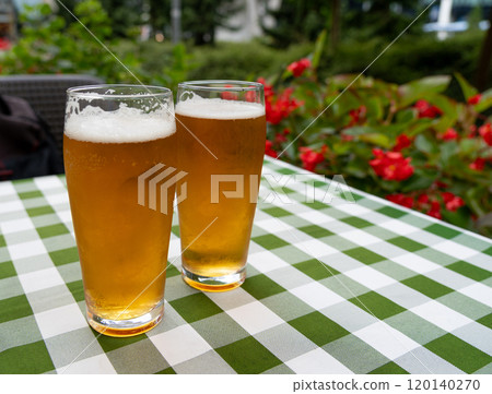 Two beer glasses at outdoor cafe, cold pint glass on checkered tablecloth table, cool condensation 120140270