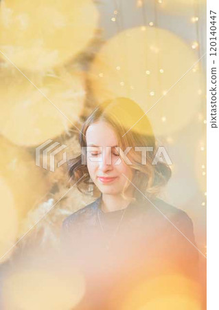 teenage girl in a dress near an unconventional Christmas tree surrounded by golden lights teenage girl in a dress near an unconventional Christmas tree surrounded by golden lights 120140447