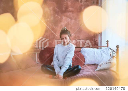 fragile teenage girl in bed hugging pillows surrounded by golden Christmas lights 120140478