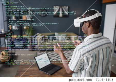 Young Black man wearing VR headset standing in living room using virtual app for coding Young Black man wearing VR headset standing in living room using virtual app for coding 120141103