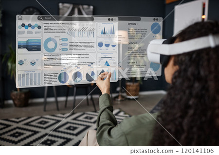 Over-the-shoulder shot of unrecognizable young woman wearing VR headset sitting in living room using app for remote work Over-the-shoulder shot of unrecognizable young woman wearing VR headset sitting in living room using app for remote work 120141106