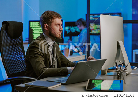 Young Caucasian male programmer working on computers at workplace in cybersecurity office, medium shot 120141165