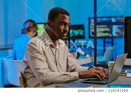Medium shot of gen Z African American cybersecurity specialist typing on laptop at work in modern office 120141169