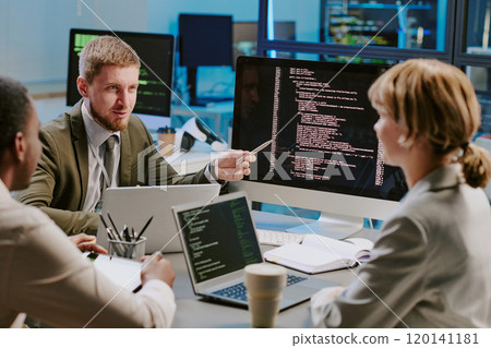 Group of three young data security specialists discussing ways of upgrading computer systems during meeting in modern office 120141181