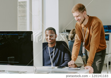 Cheerful young African American and Caucasian programmers working together on new software in leading IT company office Cheerful young African American and Caucasian programmers working together on new software in leading IT company office 120141183