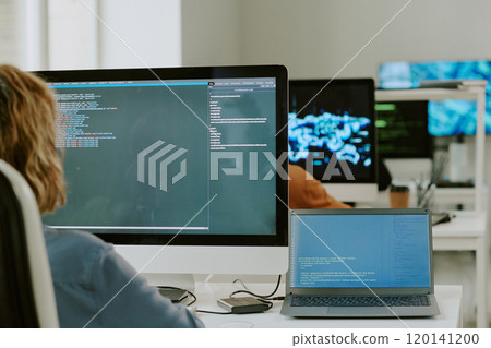Over shoulder shot of unrecognizable young woman sitting at workplace in modern IT company office, coding on desktop computer and laptop 120141200