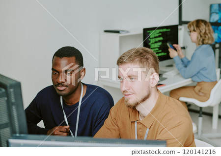 High angle view of two young ethnically diverse programmers working together on new software in modern IT company office High angle view of two young ethnically diverse programmers working together on new software in modern IT company office 120141216